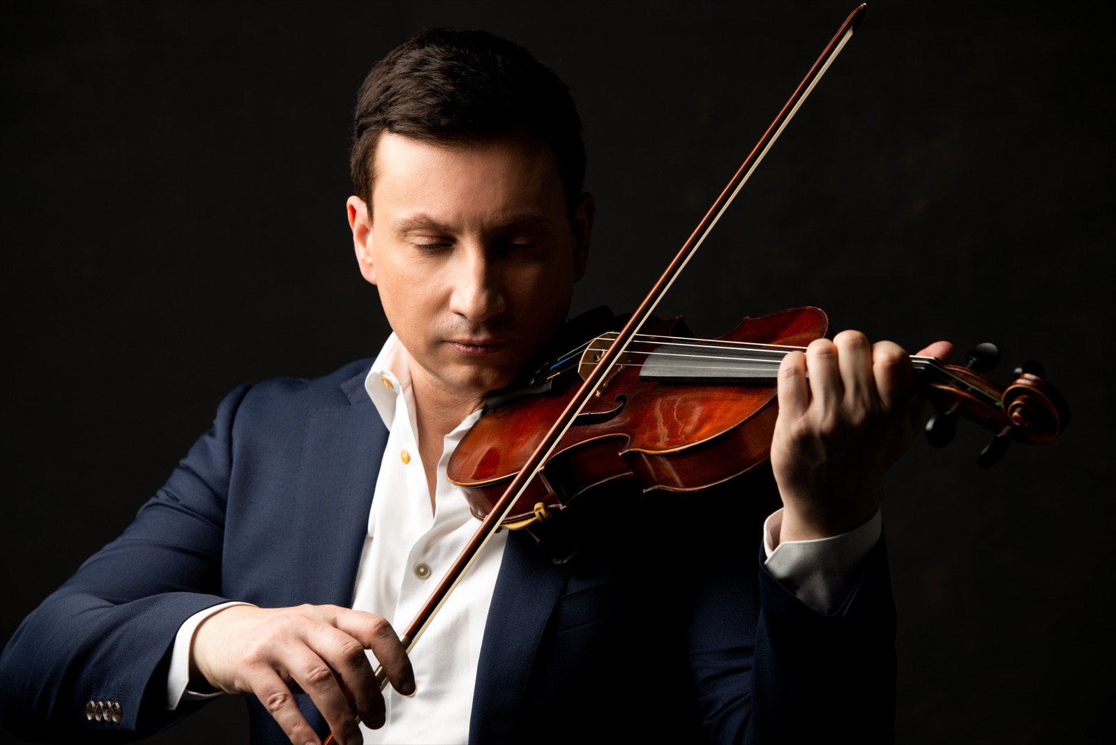 François Mathian playing the violin, facing the camera, against a dark background