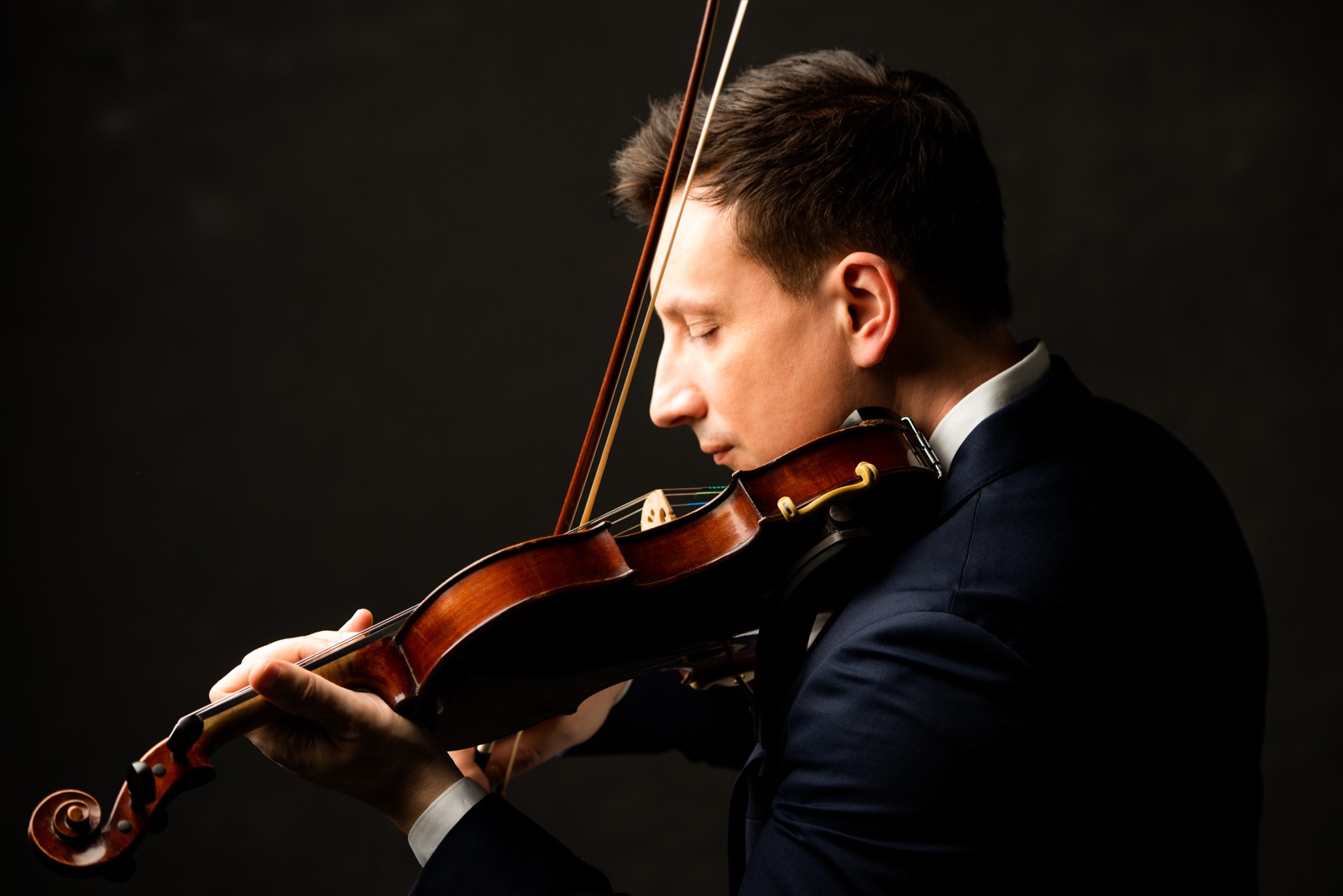 François Mathian in profile, eyes closed, playing the violin against a dark background