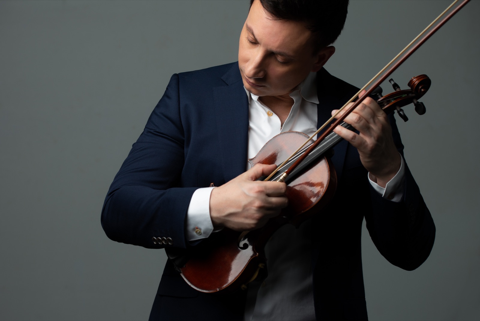 François Mathian looking down at his violin, on a grey background